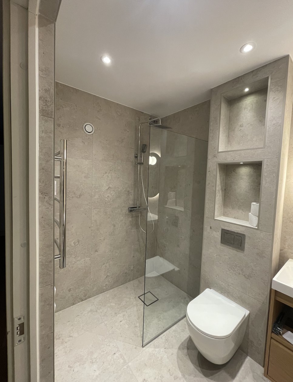 Glass walk-in shower with rain shower, linear floor drain and chrome towel rail in light limestone