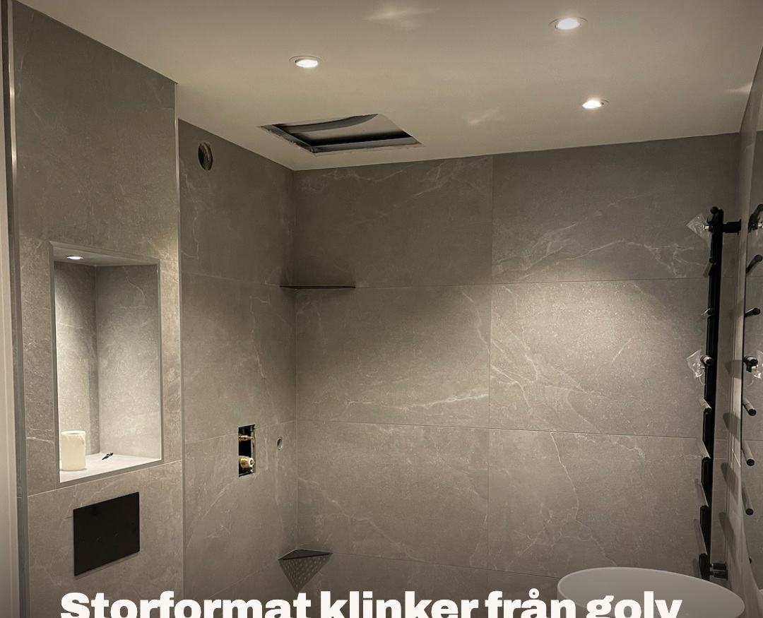 Badrum med grå storformatsplattor, belyst nisch ovanför vägghängd WC och spotlights i taket